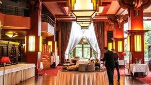 A grand hall with a red carpet, a round table with a white tablecloth, and a chandelier.