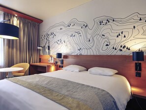 Ett hotellrum med en stor säng, två sängbord, ett skrivbord, en stol och en vägg med en topografisk karta som motiv.