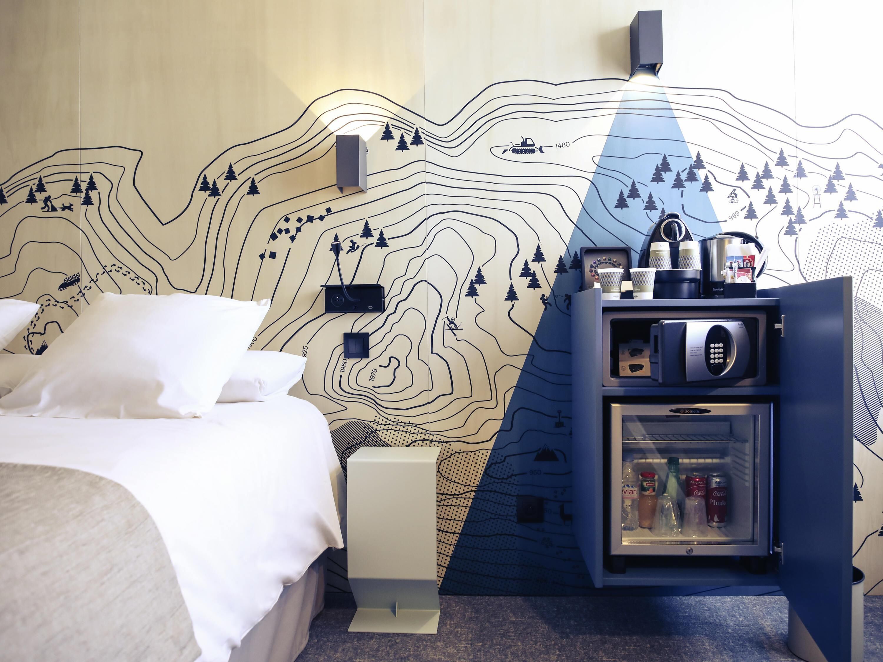 A hotel room with a bed, a refrigerator, and a wall with a topographic map design.