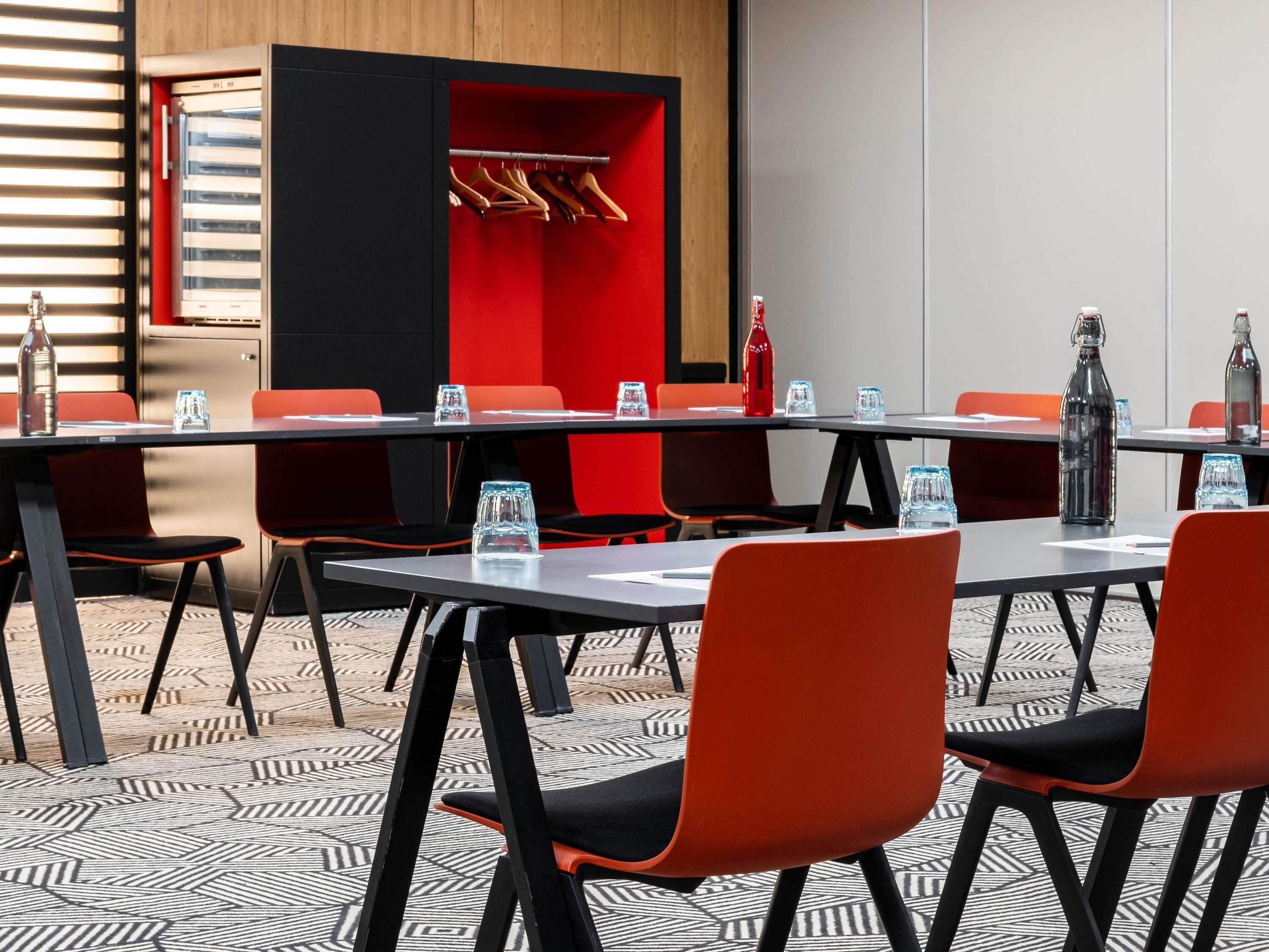 A conference room with a long table, multiple chairs, and a red accent wall.