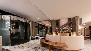 A modern interior with a marble floor, a curved sofa, a wooden bench, and a staircase with a wooden railing. - Mercure Grenoble Centre Alpotel (Grenoble)