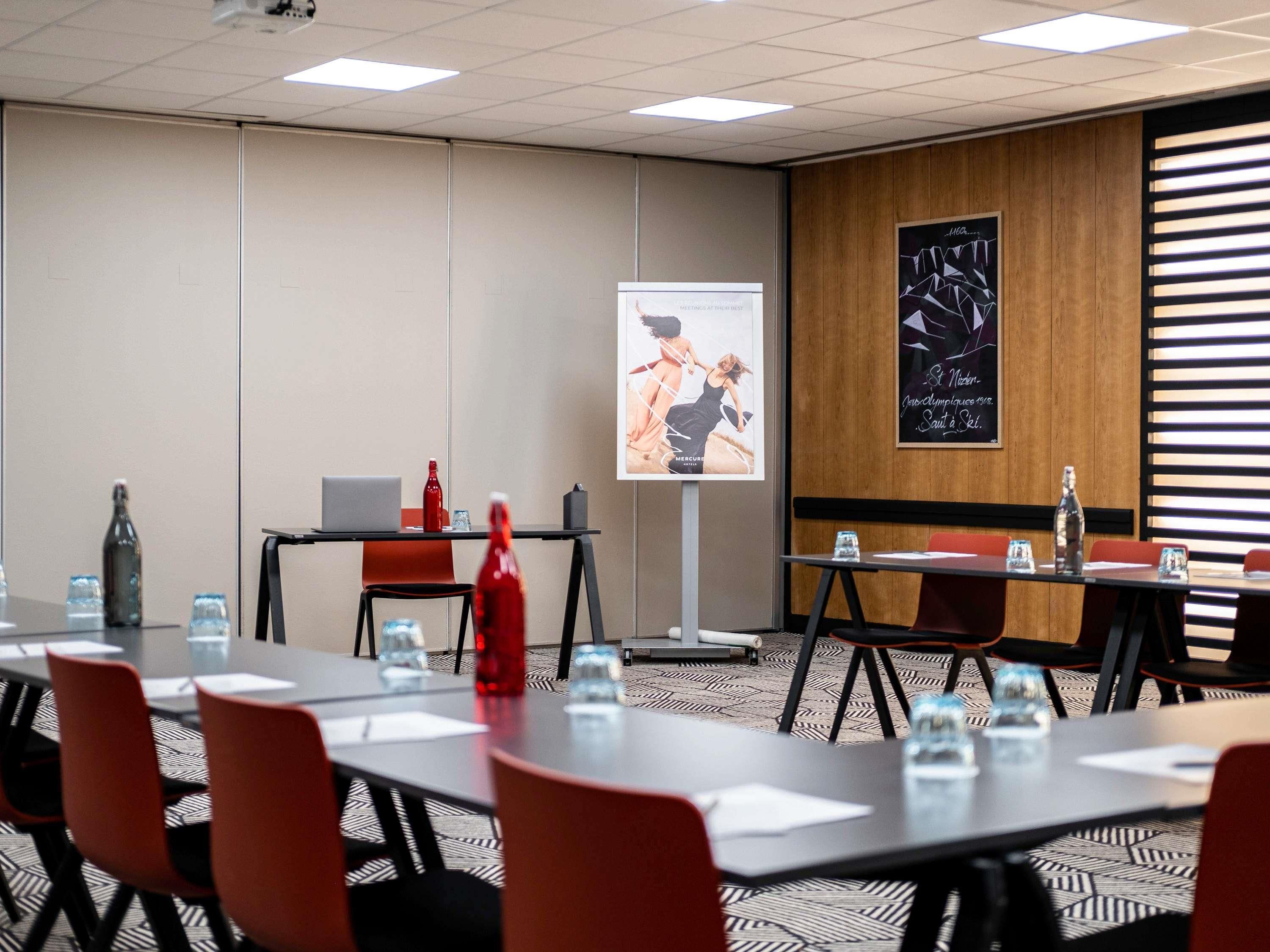 A conference room with tables, chairs, a projector screen, and a poster on the wall.