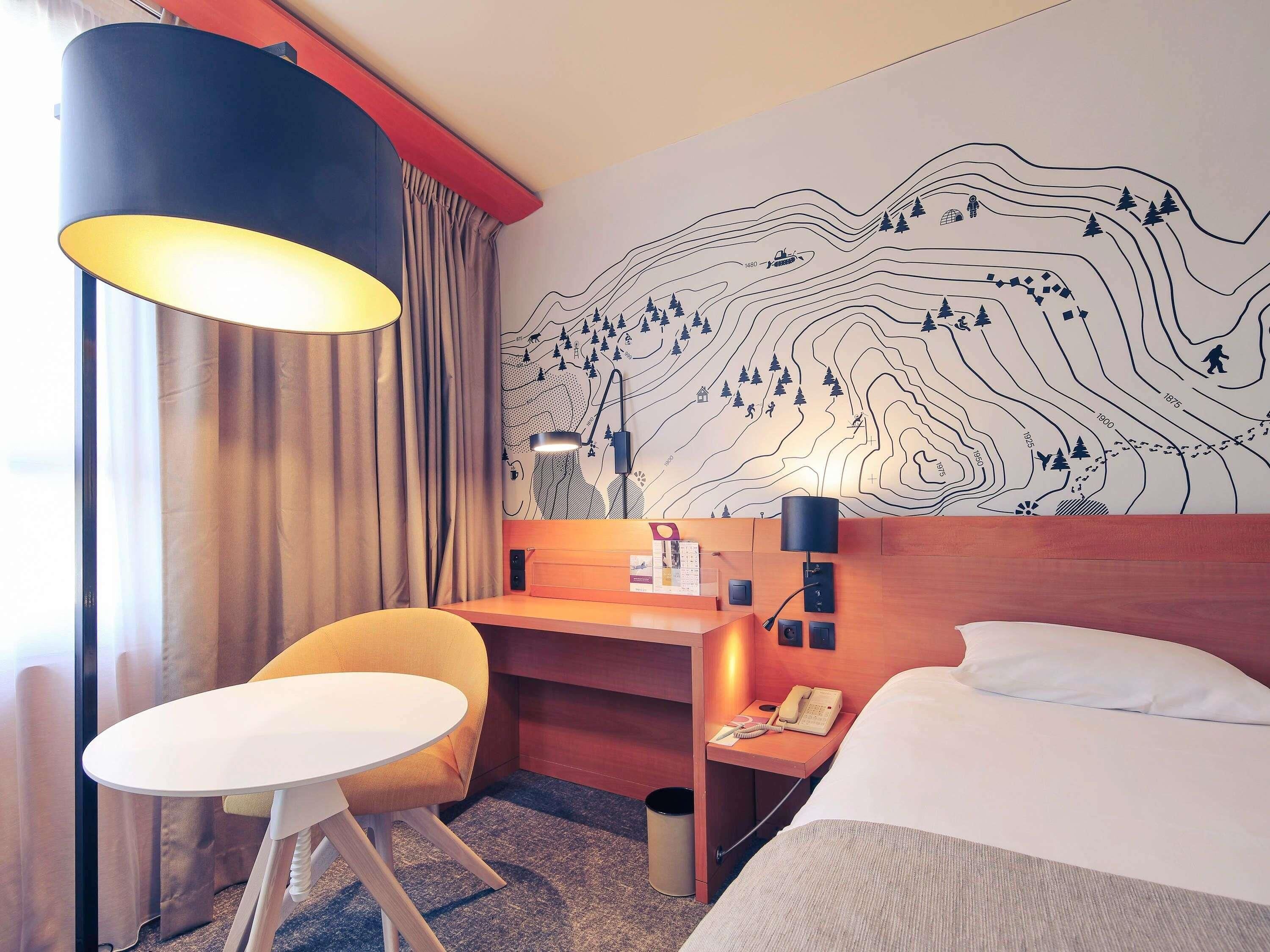 Ein Hotelzimmer mit einem Bett, einem Schreibtisch, einem Stuhl, einer Lampe und einer Wand mit einer topografischen Kartenlandschaft.