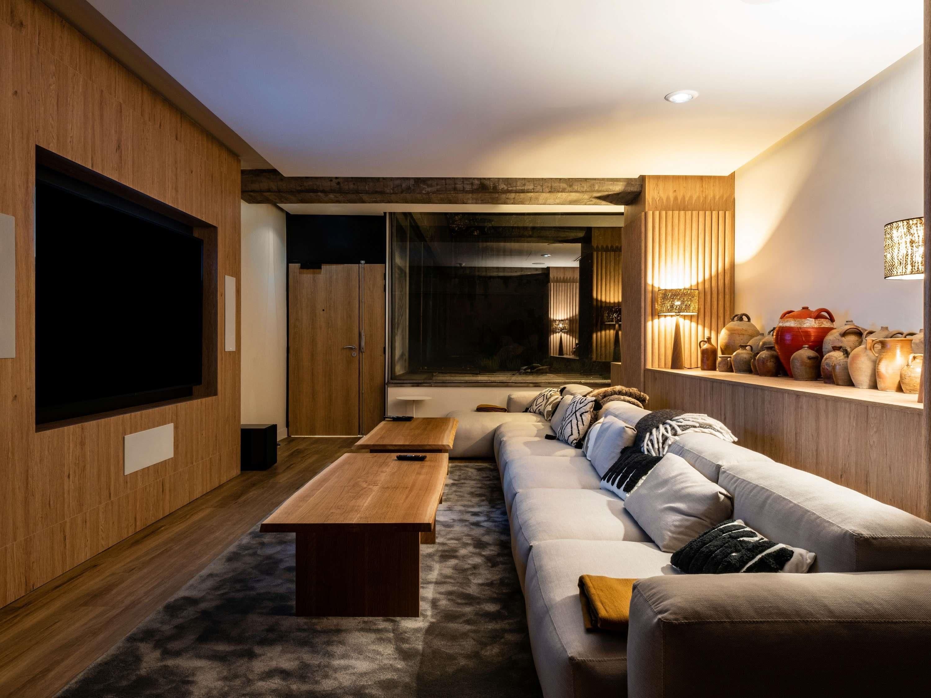 Ein modernes Wohnzimmer mit großem Flachbildfernseher, einem Holztisch, einer Couch mit Kissen und einem Kamin.