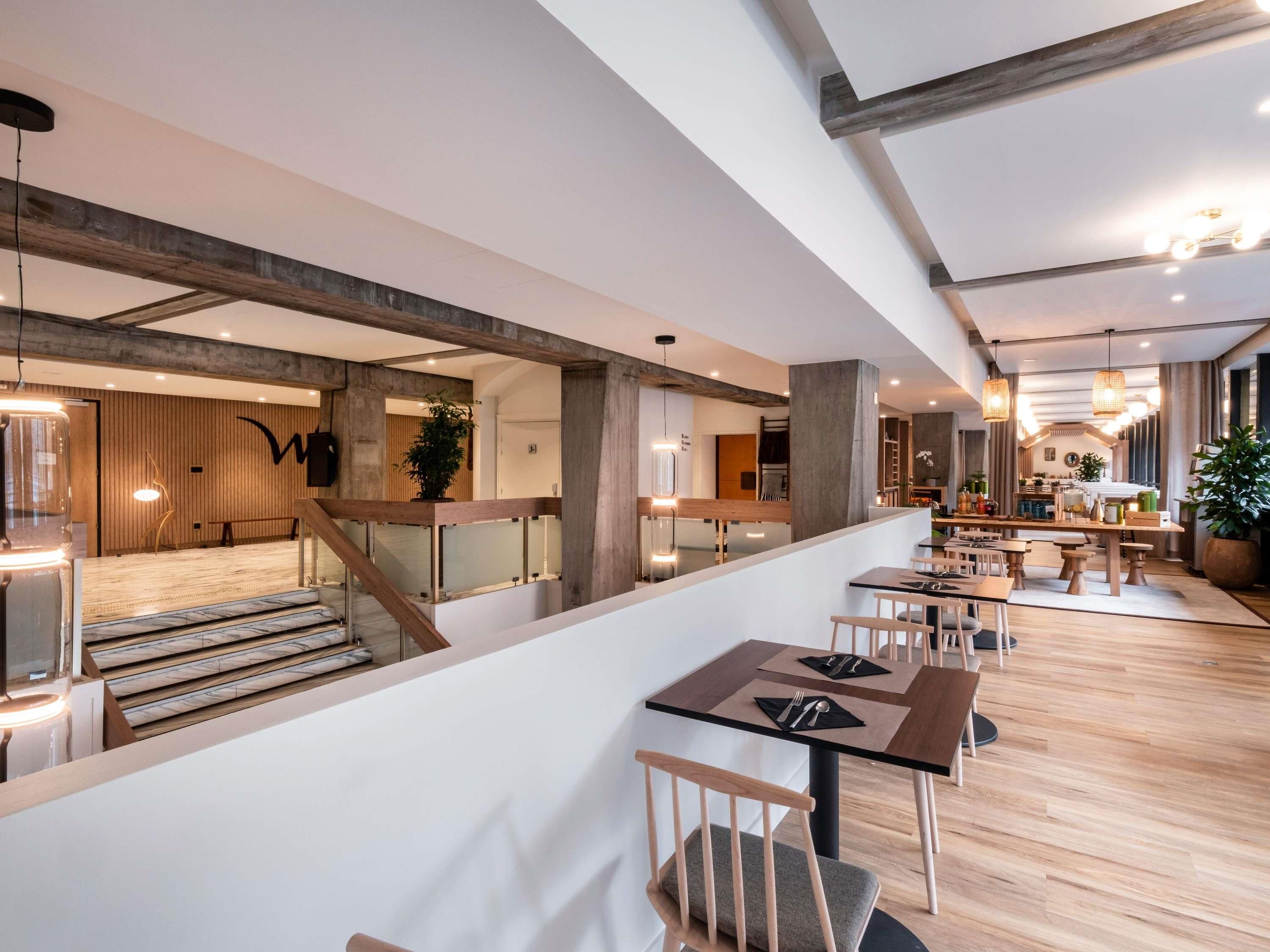 A modern restaurant with a high ceiling, exposed beams, and a central bar area.