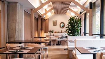 Un interior de restaurante moderno con vigas de madera, mesas redondas y una planta grande en maceta.
