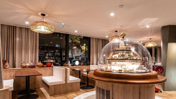 A modern interior with a central round table, wooden flooring, and a view of the street outside. - Mercure Grenoble Centre Alpotel (Grenoble)