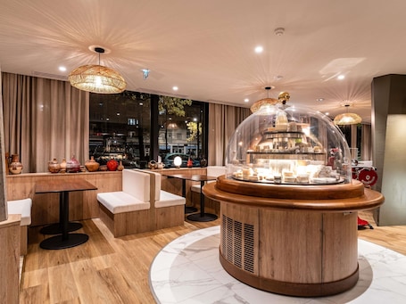 A modern interior with a central round table, wooden flooring, and a view of the street outside.. Mercure Grenoble Centre Alpotel