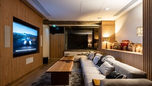 A modern living room with a large flat-screen TV, a wooden coffee table, a sofa, and a shelf with decorative items. - Mercure Grenoble Centre Alpotel (Grenoble)