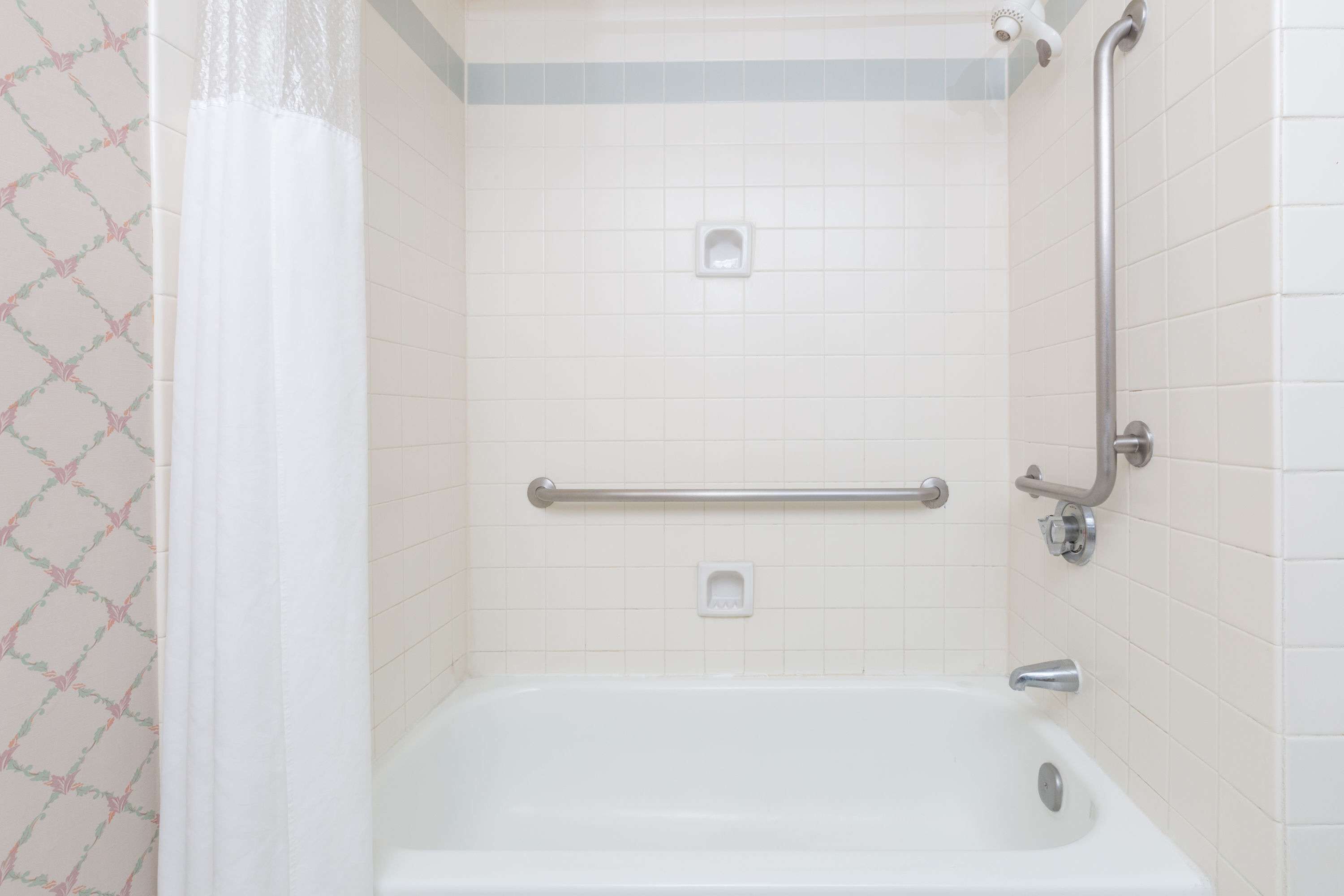 Un baño con una bañera blanca, barras de apoyo y una cortina de ducha.