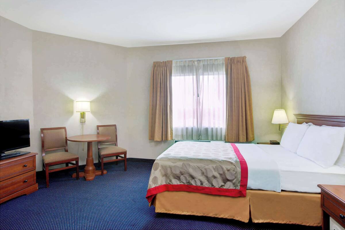 A hotel room with a bed, a television, a desk, two chairs, and a window with curtains.