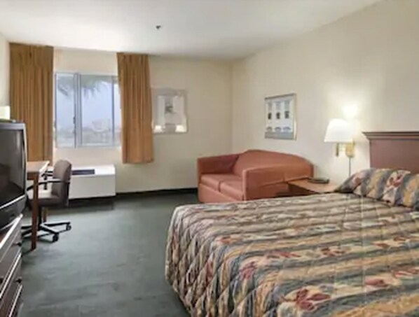Habitación de hotel con cama, escritorio, silla, televisor y ventana con cortinas.