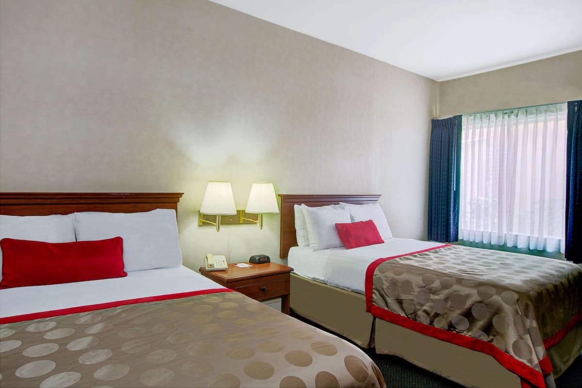 A hotel room with two beds, a nightstand, a telephone, and a window with curtains.
