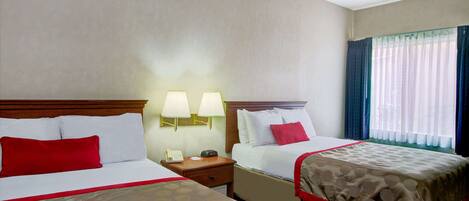 A hotel room with two beds, a nightstand, a telephone, and a window with curtains.