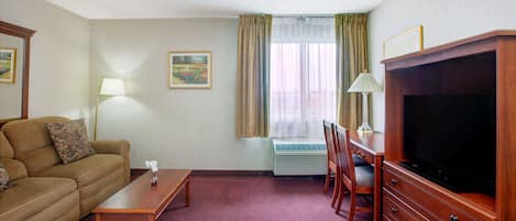 A hotel room with a sofa, a wooden desk, a television, a lamp, and a window with curtains.