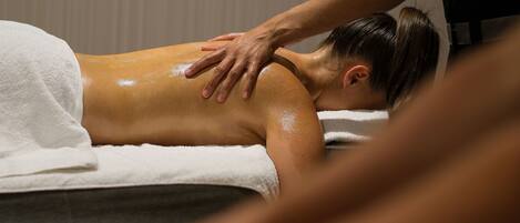 A massage therapy session in progress with a client lying face down on a massage table, covered with a white towel.
