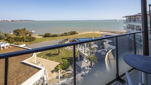 Un balcon avec vue sur la mer, une piscine et un immeuble à plusieurs étages.