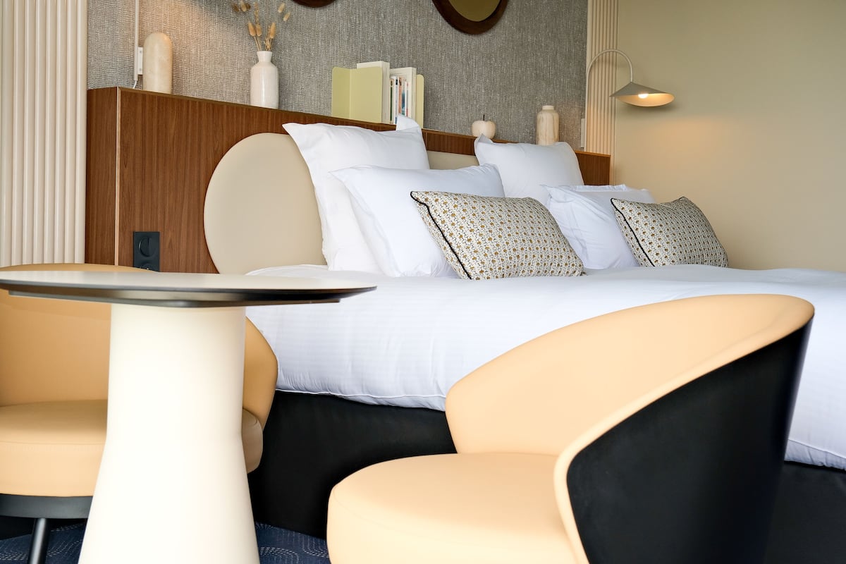 Una habitación de hotel moderna con una cama bien hecha, una mesita redonda pequeña y dos sillas.