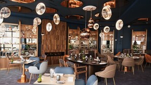 Un intérieur de restaurant moderne avec des tables rondes, des chaises rembourrées en tissu bleu et une variété de luminaires suspendus.