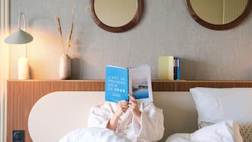 Una persona leyendo un libro en una habitación de hotel con cabecera de madera, una lámpara de noche y un espejo en la pared.