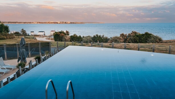 Une piscine à débordement offrant une vue sur l’océan et une côte lointaine.