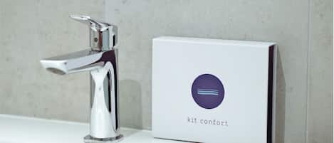 A modern bathroom with a chrome faucet and a white box labeled "kit confort" on a white countertop.