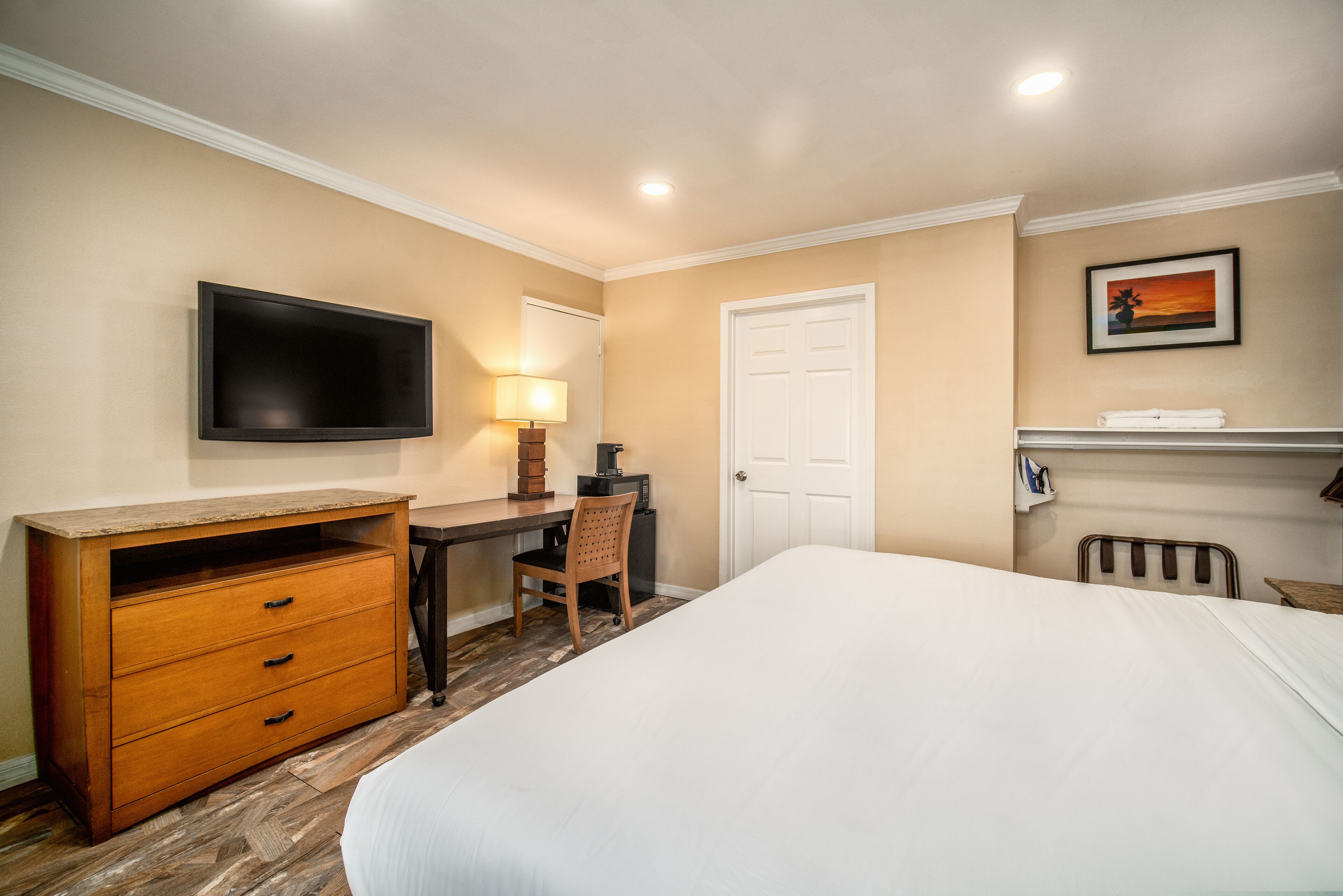 Une chambre d’hôtel avec un lit, un bureau et une chaise, une télévision, une lampe et une porte.