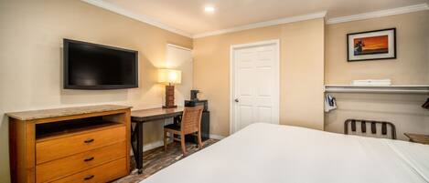 A hotel room with a bed, a desk with a chair, a television, a lamp, and a door.