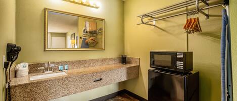 A bathroom with a sink, mirror, vanity, and a microwave.