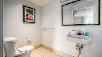 Un baño con inodoro, lavamanos con artículos de aseo, un cuadro en la pared y un espejo.