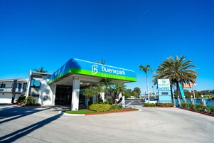 Un hotel con un llamativo letrero que dice 'Buenapark Hotel & Suites', un estacionamiento y palmeras.