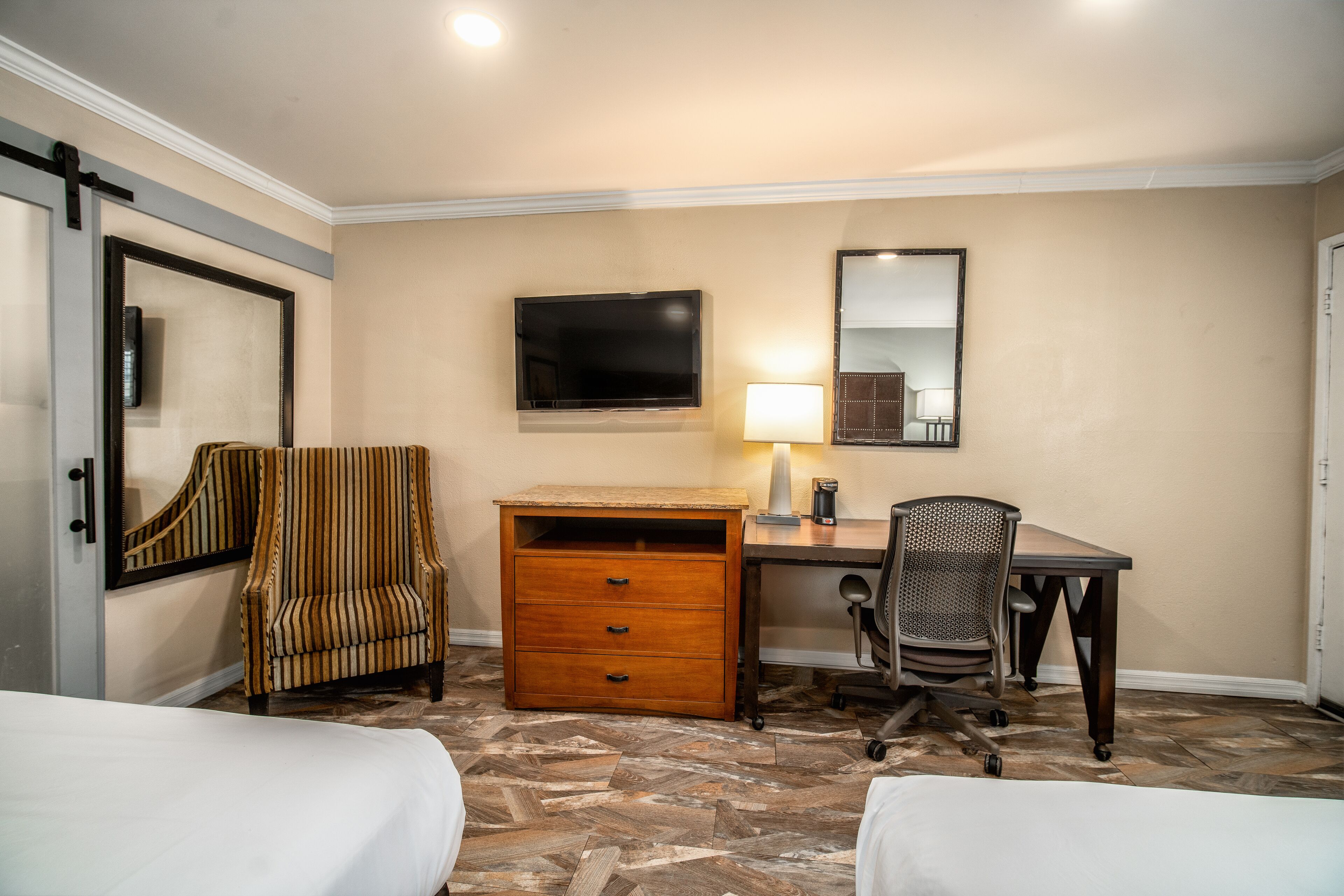 A hotel room with a bed, a desk, a chair, a dresser, a TV, and a lamp.