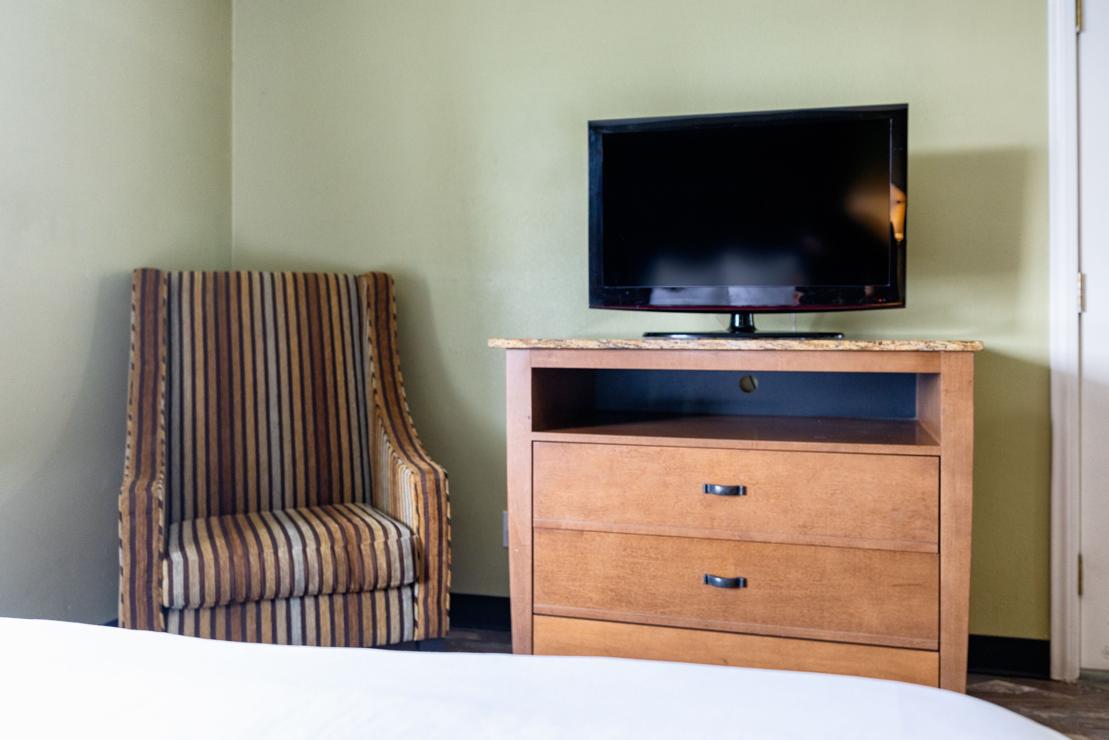 Una habitación de hotel con una televisión sobre un mueble de madera, un sillón a rayas y una cama.