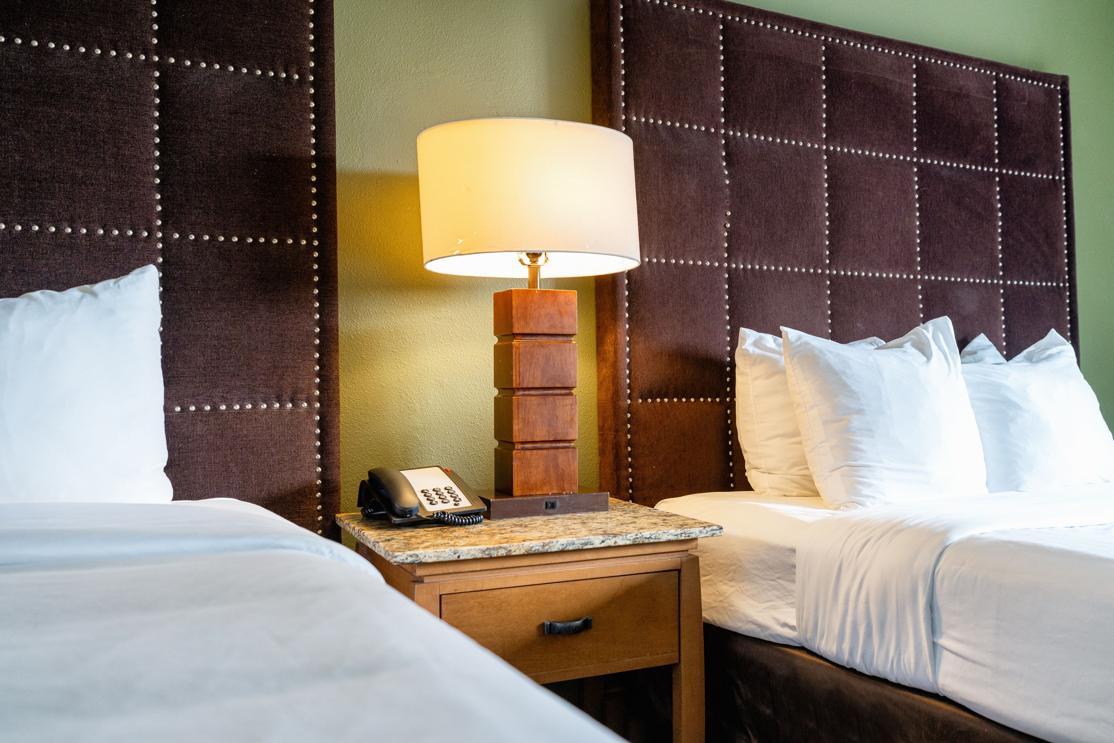 A hotel room with two beds, a nightstand with a lamp, a telephone, and a drawer.