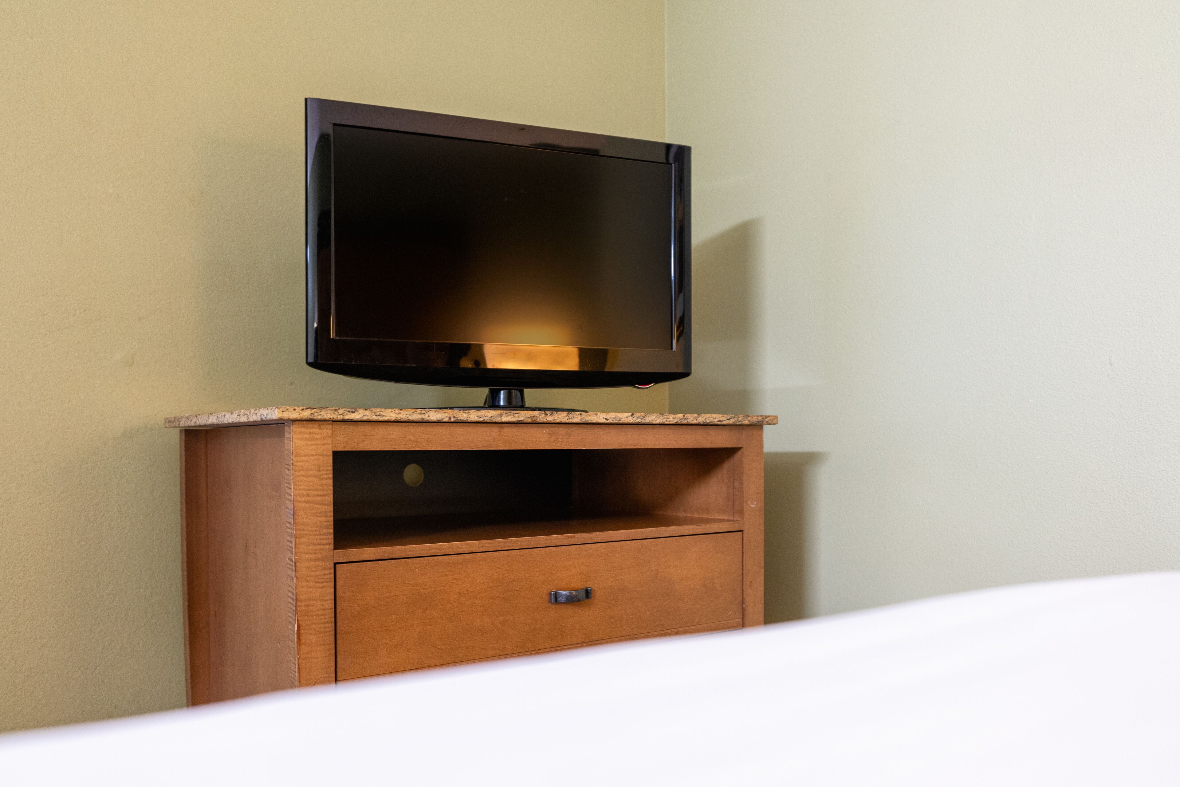 A TV on a wooden cabinet with a drawer below it.