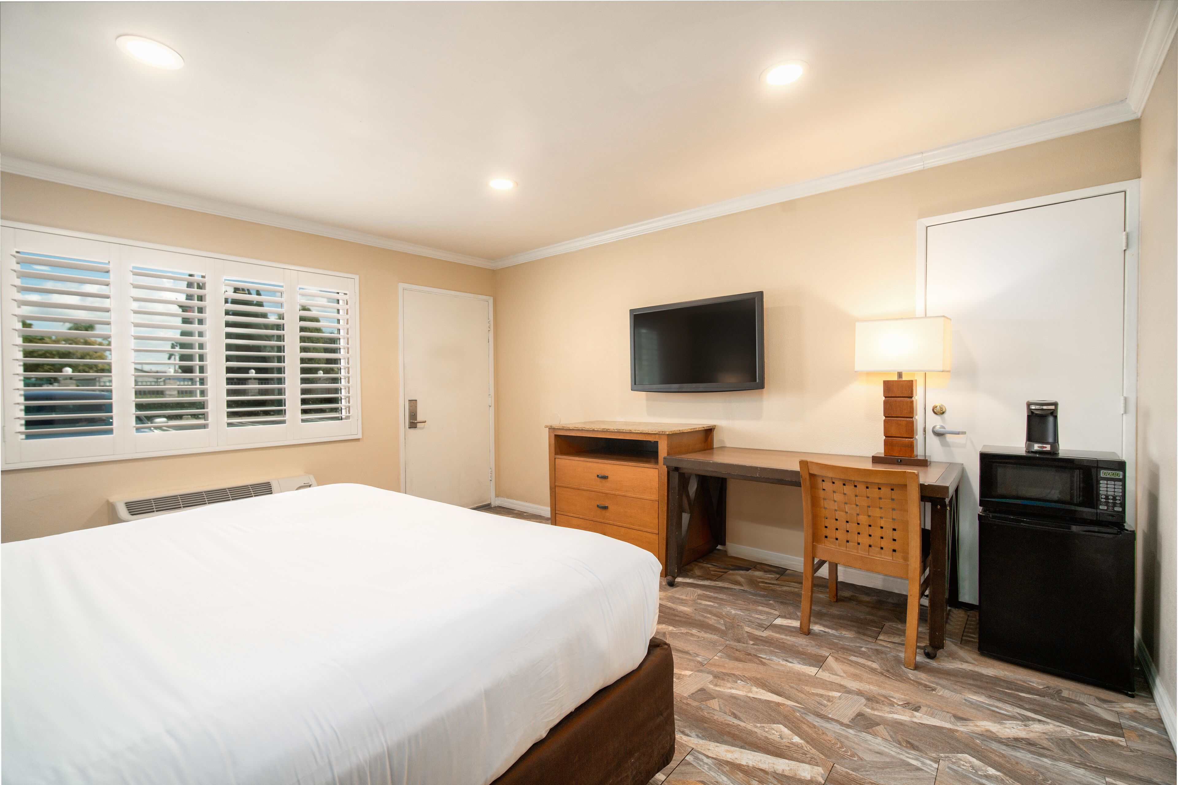 A bedroom with a bed, a desk, a chair, a television, a lamp, and a refrigerator.