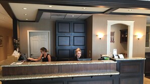A reception desk with two staff members, a dark wood paneling design, and a light fixture on the wall. - Heritage Hotel Lancaster (Lancaster)