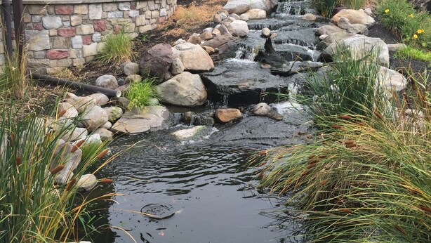 A small stream with rocks and plants, a stone wall, and a wooden structure with a spiral staircase. - Heritage Hotel Lancaster (Lancaster)