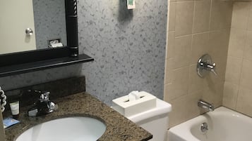 A bathroom with a granite countertop sink, a white toilet, a bathtub, and a wall-mounted light fixture.