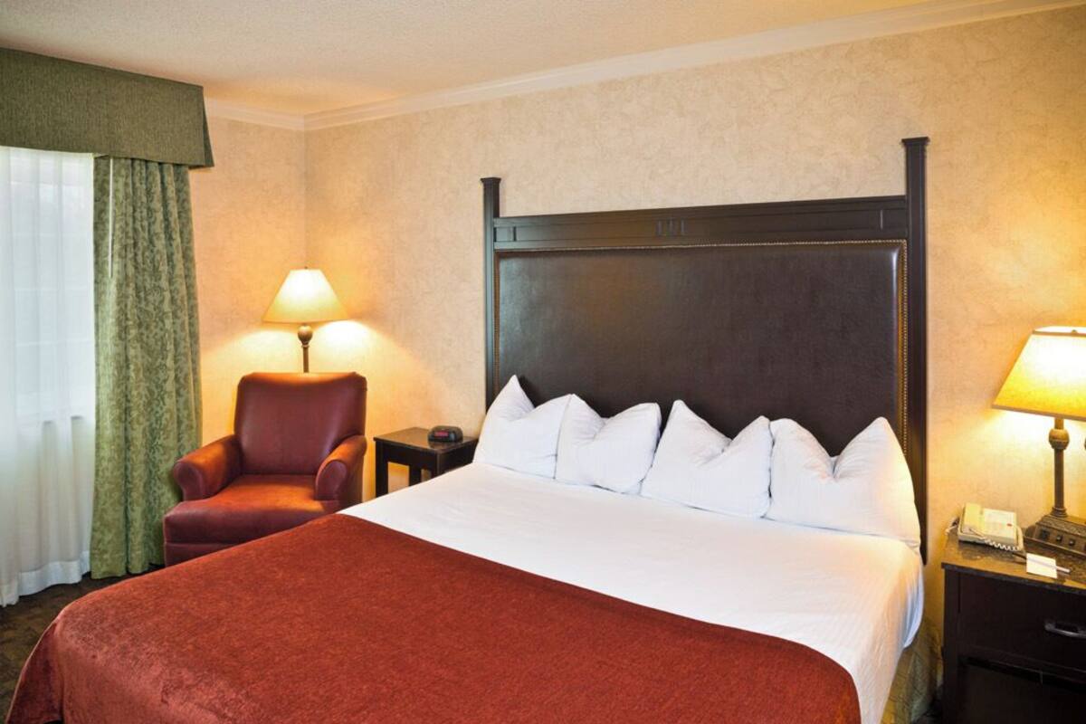 A hotel room with a large bed, a chair, two bedside tables with lamps, and a window with curtains.
