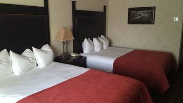 Habitación de hotel con dos camas, cada una con ropa blanca y mantas rojas. Se ve una mesita de noche con una lámpara y un teléfono.
