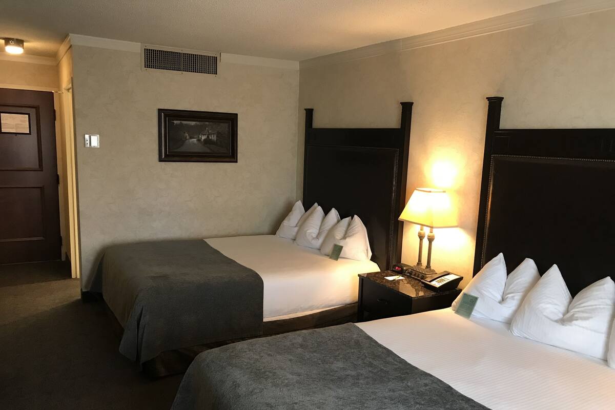 A hotel room with two beds, a nightstand with a lamp, a framed picture on the wall, and a door.