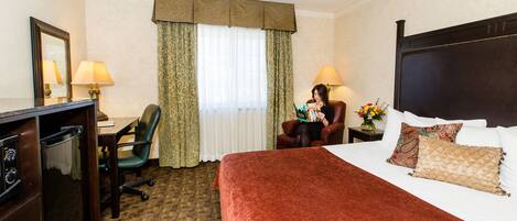 A hotel room with a bed, a desk, a chair, and a dresser.