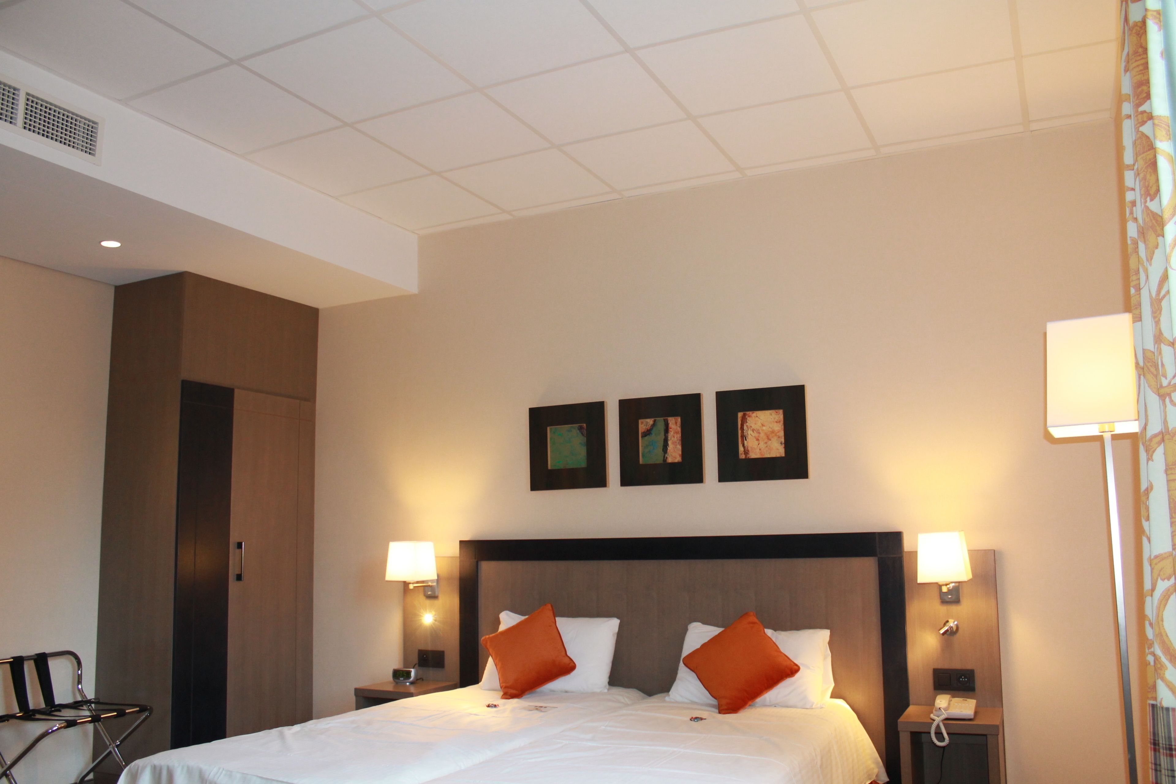 Ein Hotelzimmer mit einem großen Bett, zwei Nachttischlampen, einem Nachttisch, einem Sessel und einem Kleiderschrank.