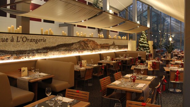 A restaurant with booths and tables, a Christmas tree, and candles on the wall. - Castel de Pont-à-Lesse Hotel (Dinant)