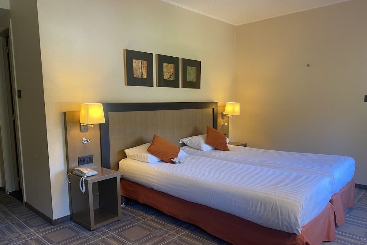 A hotel room with a large bed, two bedside tables with lamps, a telephone, and three framed pictures on the wall.