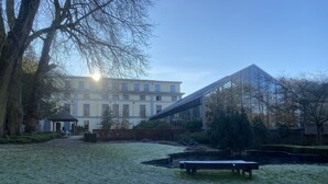A building with a glass facade and a garden area with a bench and a small pond. - Castel de Pont-à-Lesse Hotel (Dinant)