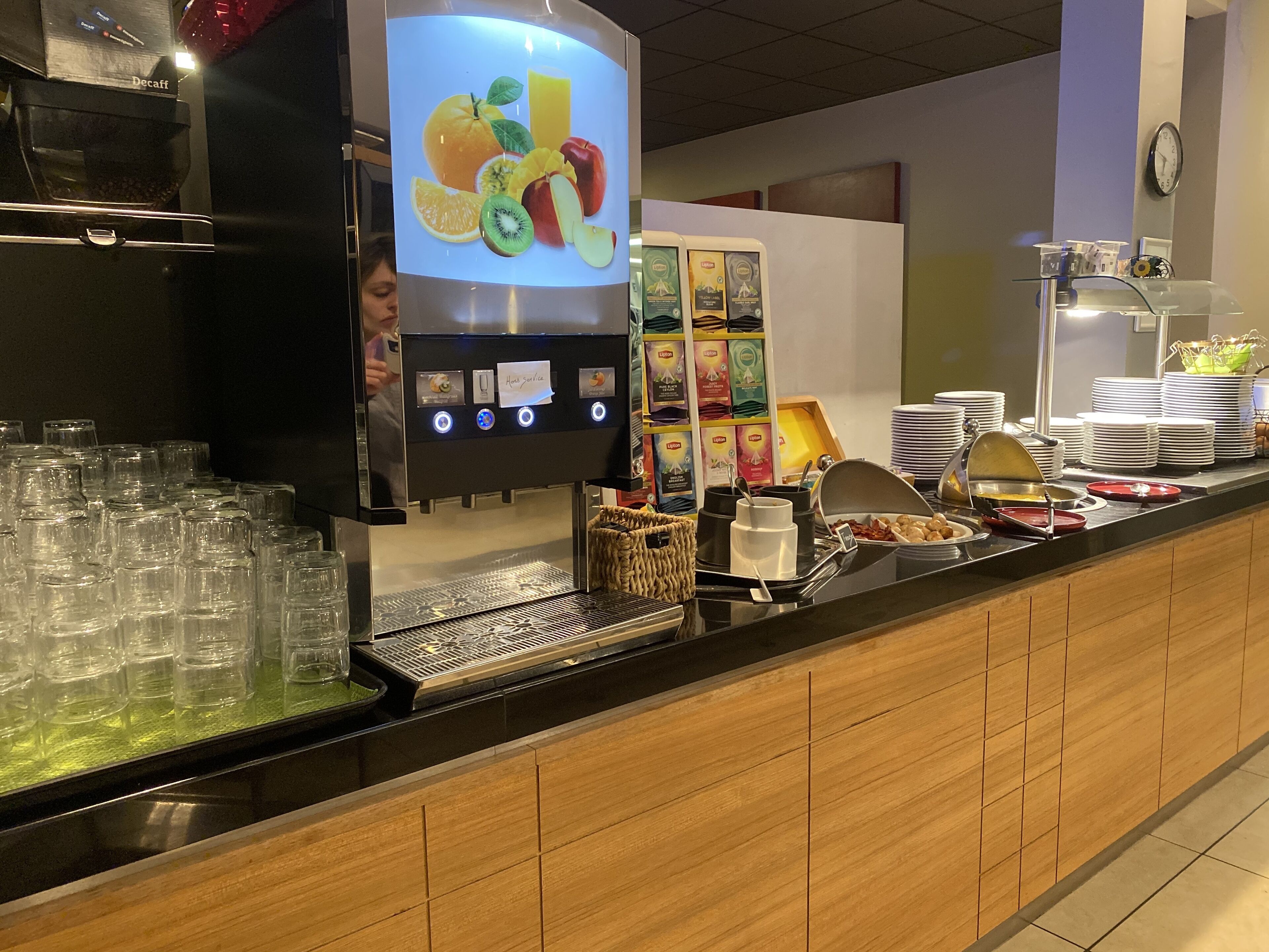 Zona de bufé con dispensador de bebidas, platos apilados y diversos recipientes de comida.