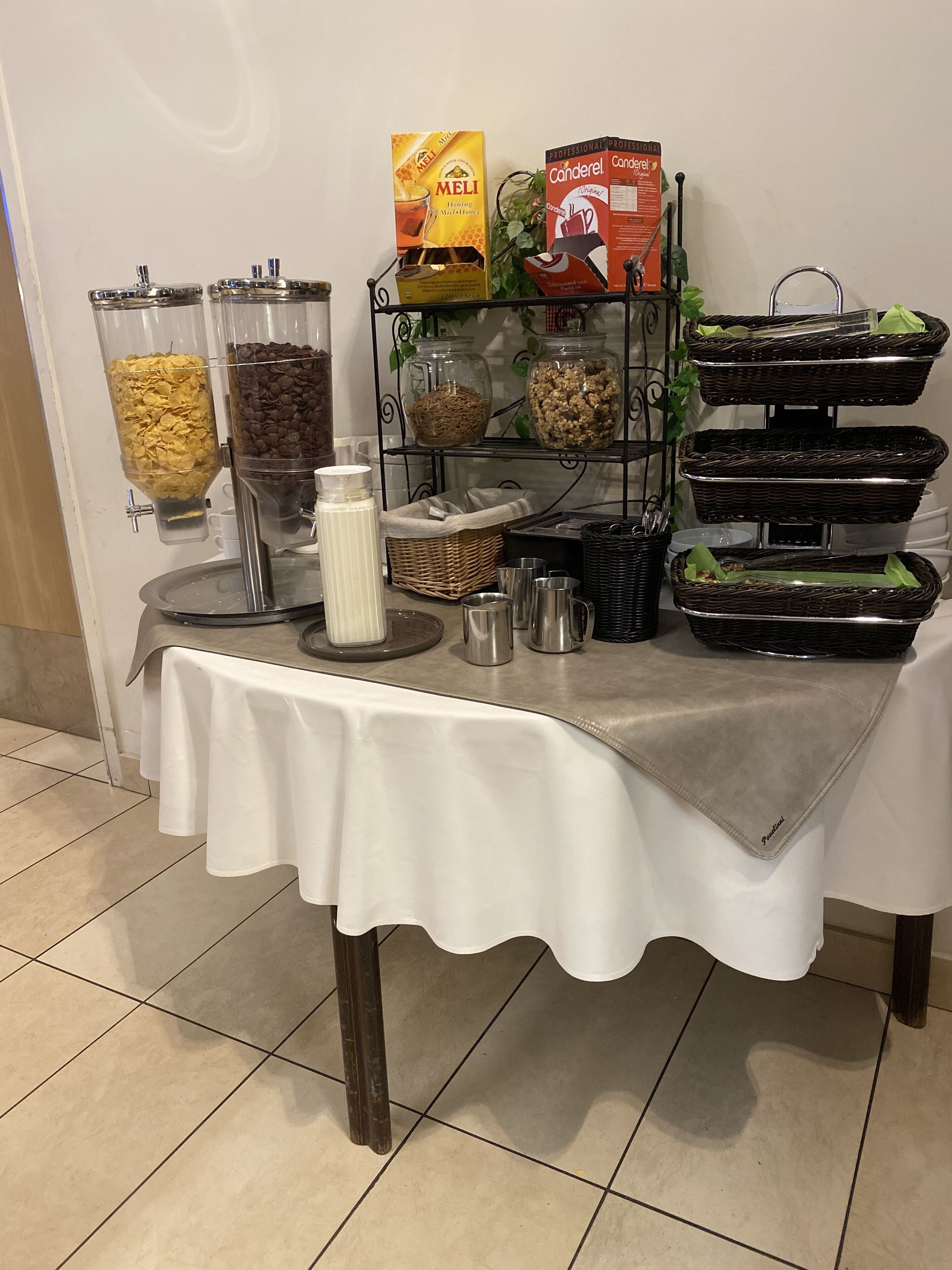 Une table de buffet proposant divers aliments et contenants, notamment des céréales, du café et des condiments.