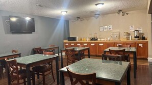 A dining area with tables and chairs, a kitchen counter with appliances, and a flat-screen TV mounted on the wall.